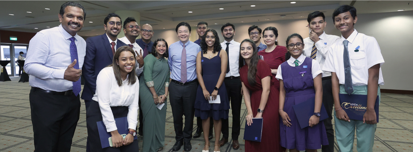 Group of people in formal wear and school uniforms holding SINDA Excellence Awards certificates.